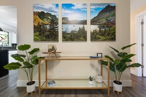 Et værelse med et trækonsolbord, potteplanter og tre landskabsmalerier på væggen.
