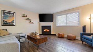 A living room with a fireplace, a sofa, a coffee table, and a TV mounted on the wall. - Glacier Getaway! Huge Home! Sleeps 14! (Columbia Falls)