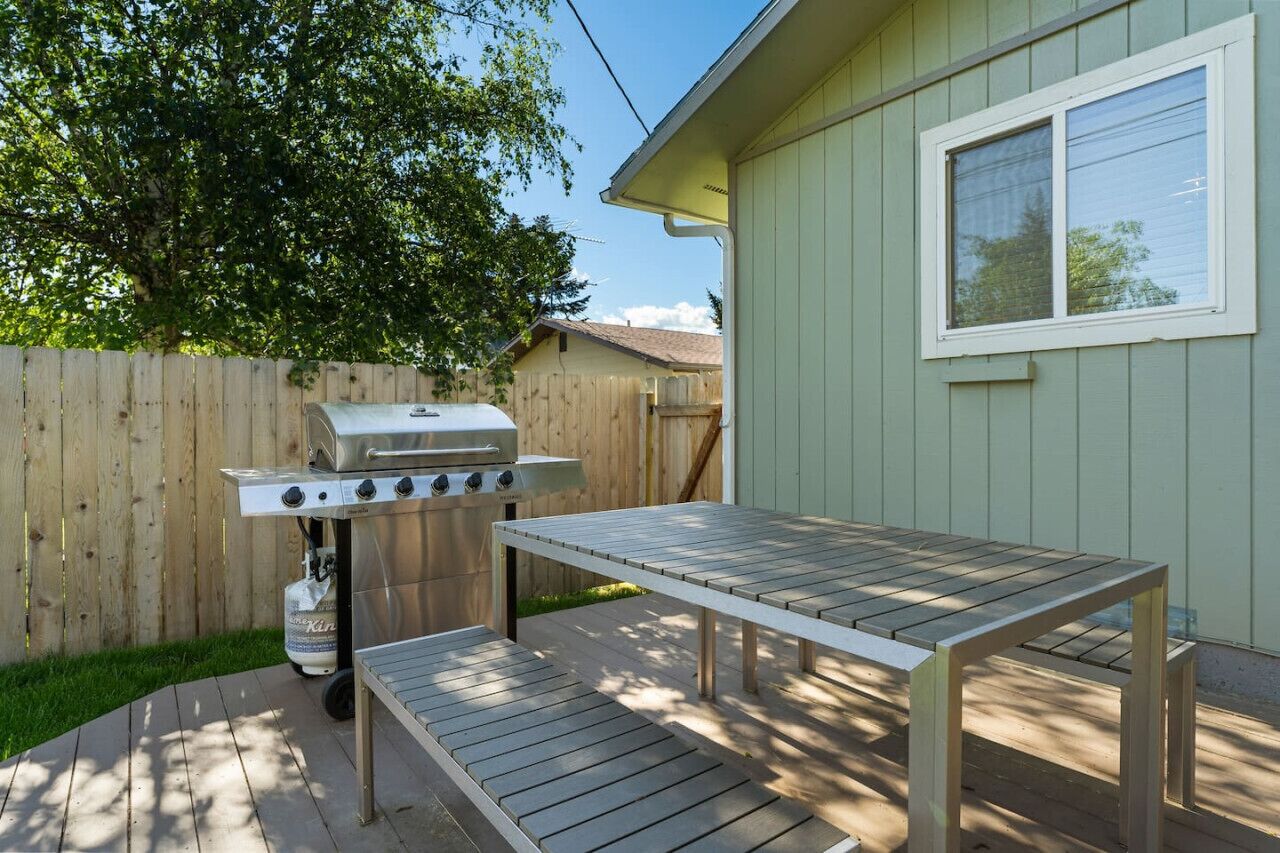 A backyard with a wooden grill, a picnic table, and a house with a window.