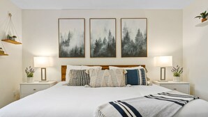 A neatly arranged bedroom with a large bed, two bedside tables with lamps, and three framed forest landscape paintings on the wall. - Glacier Getaway! Huge Home! Sleeps 14! (Columbia Falls)