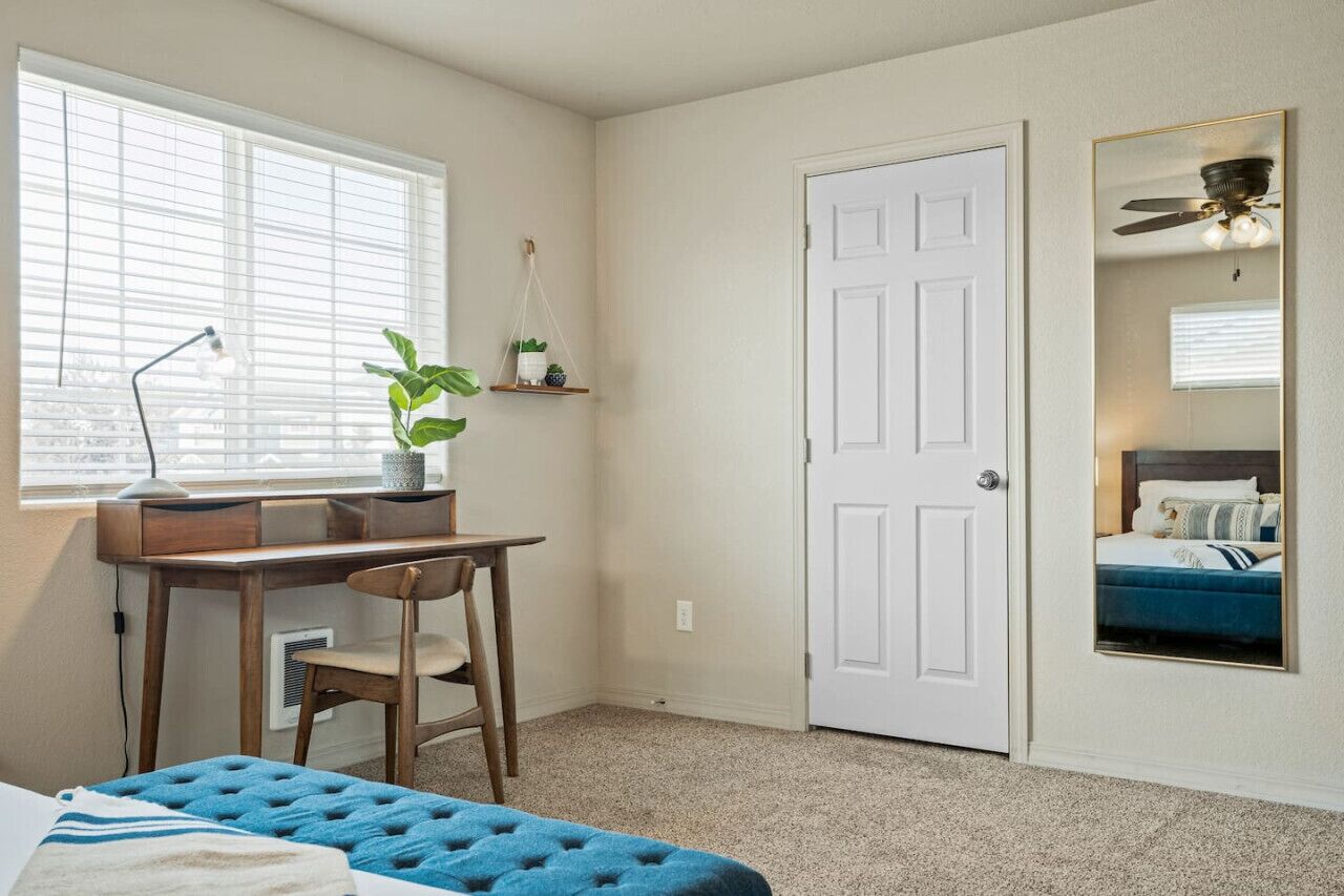 Une chambre à coucher avec un lit, un bureau, une chaise, une fenêtre et une porte.