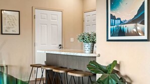 Een keuken met een witte deur, een bar met krukken en een lijst met een foto aan de muur.
