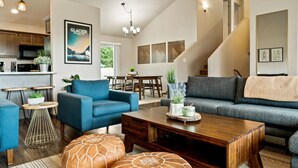 Een ruime woonkamer met een blauwe bank, een houten salontafel en een trap naar een hoger gelegen verdieping.