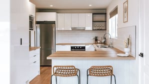 A modern kitchen with white cabinetry, a stainless steel refrigerator, a wooden countertop, and two wicker bar stools. - Wombat Hollow - Holiday Houses Tasmania (Swansea)