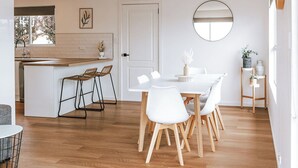 A modern kitchen with a central island, white bar stools, a round mirror, and a dining table with chairs. - Wombat Hollow - Holiday Houses Tasmania (Swansea)