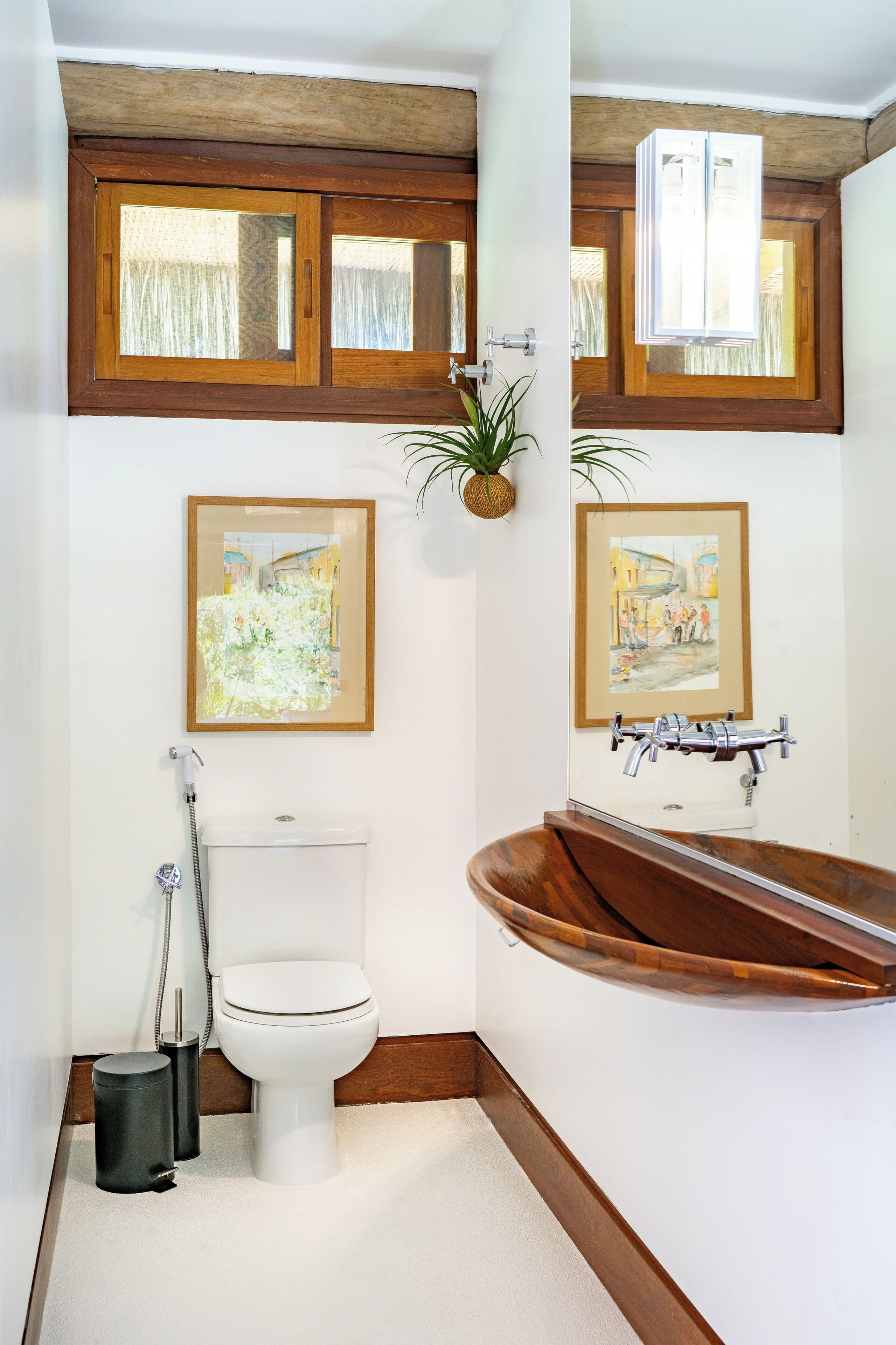 Un baño con inodoro blanco, tocador de madera y una bañera grande. Hay cuadros en la pared y una planta sobre el tocador.