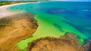 Eine Luftaufnahme einer Küstenlandschaft mit klarem türkisblauem Wasser, einem Sandstrand und Booten, die in der Nähe der Küste vor Anker liegen.