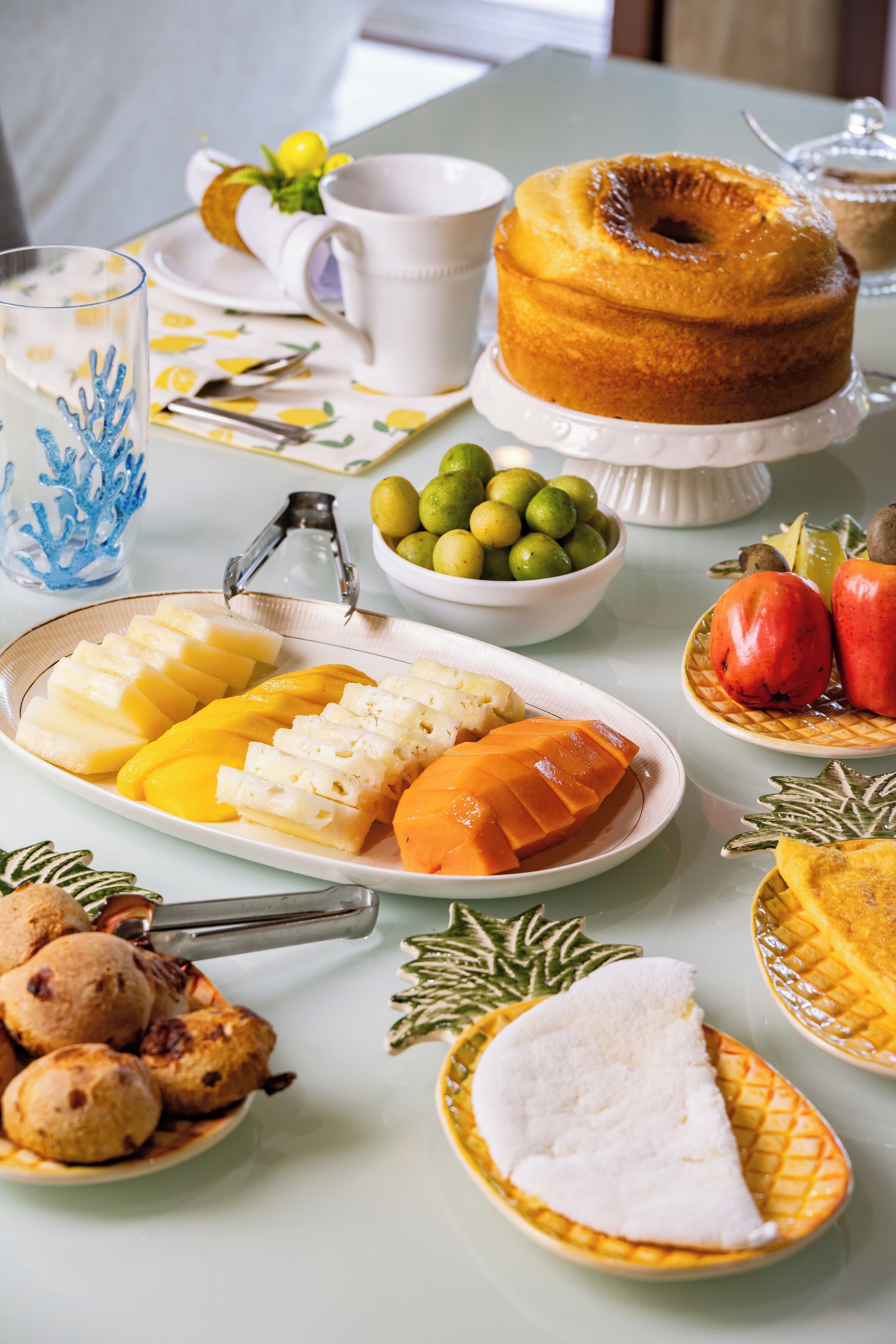 Una mesa servida con diversos platos, incluyendo un pastel Bundt, frutas en rodajas y un bol de aceitunas.