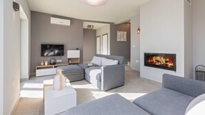 A modern living room with a flat-screen TV, grey sofas, a fireplace, and a ceiling light. - Villa Soleil in peaceful location with a sea view (Mali Kosi)