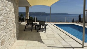 A poolside area with a stone wall, two chairs, and a yellow shade sail. - Angel Marie Villa in a calm location with sea-view (Veli Kosi)