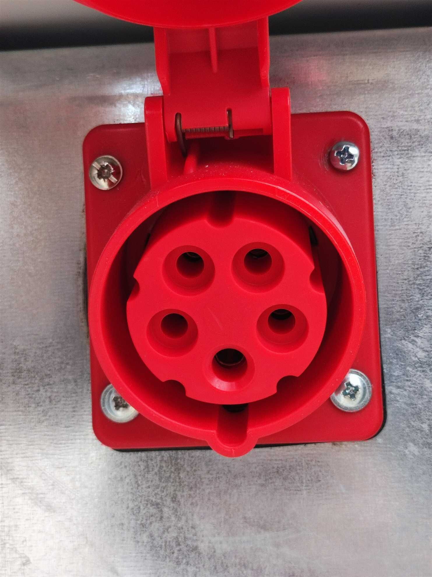 A red electrical plug with a circular connector, mounted on a metal surface with four screws.