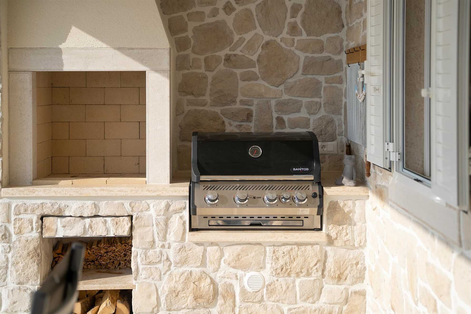 A stone-built outdoor grill area with a built-in brick oven and a window to the right.
