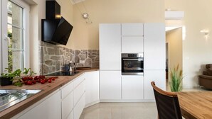 A modern kitchen with a stone backsplash, built-in oven, and a wooden dining table. - Angel Marie Villa in a calm location with sea-view (Veli Kosi)