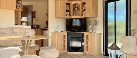 A compact living space with a kitchenette, a television, and a seating area with a table and ottomans.