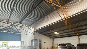 A large industrial warehouse with a corrugated metal roof, concrete floor, and two parked cars. - Hotel Inambu (Villavicencio)
