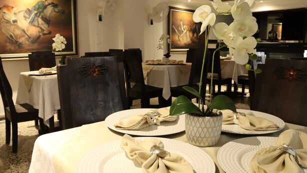A dining area with tables set for four, each with a folded napkin and a white orchid in a patterned pot. - Hotel Inambu (Villavicencio)