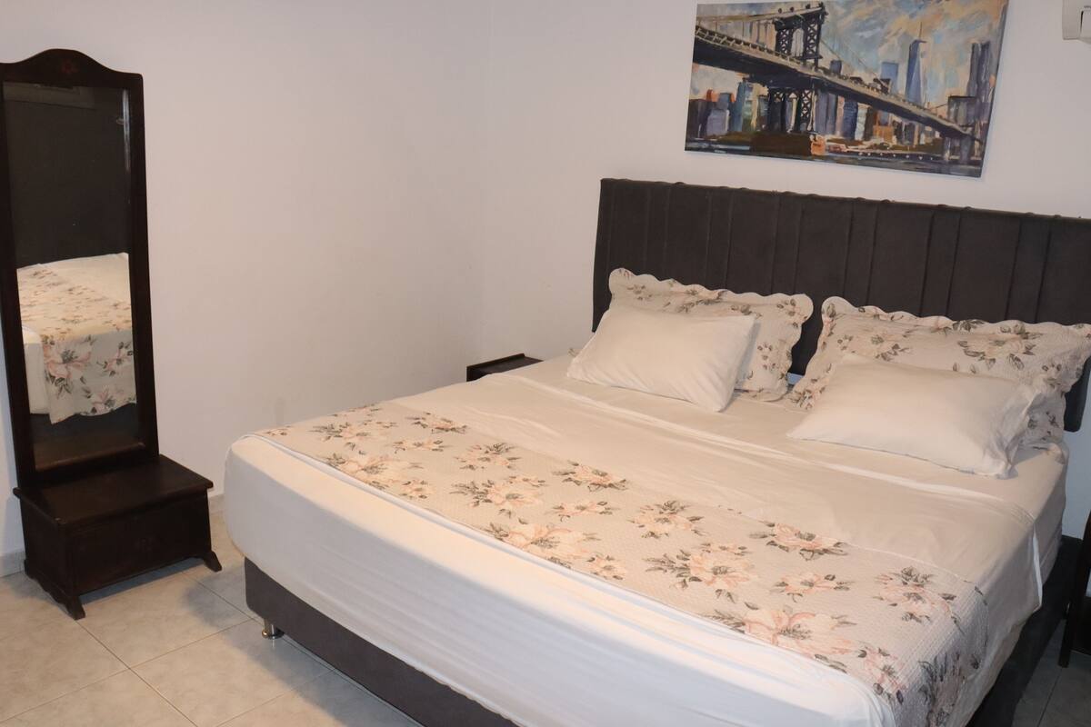 Un dormitorio con cama, mesita de noche, cómoda y un cuadro en la pared.