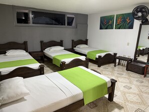 Three single beds with wooden headboards and white bedding, a wall-mounted fan, and a large window with a view of the night sky.