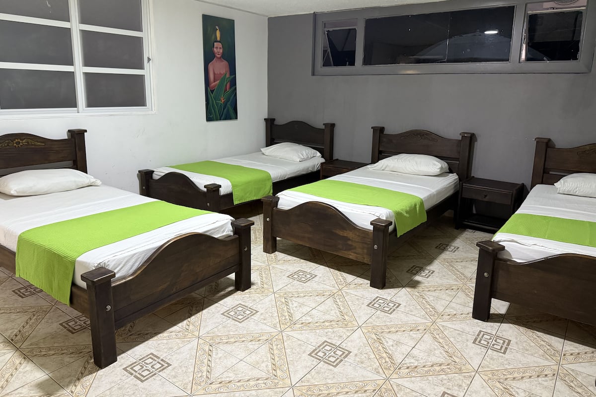 Four comfortable beds with white mattresses and green bedspreads line the room, which features a patterned tile floor and a window with an outside view.