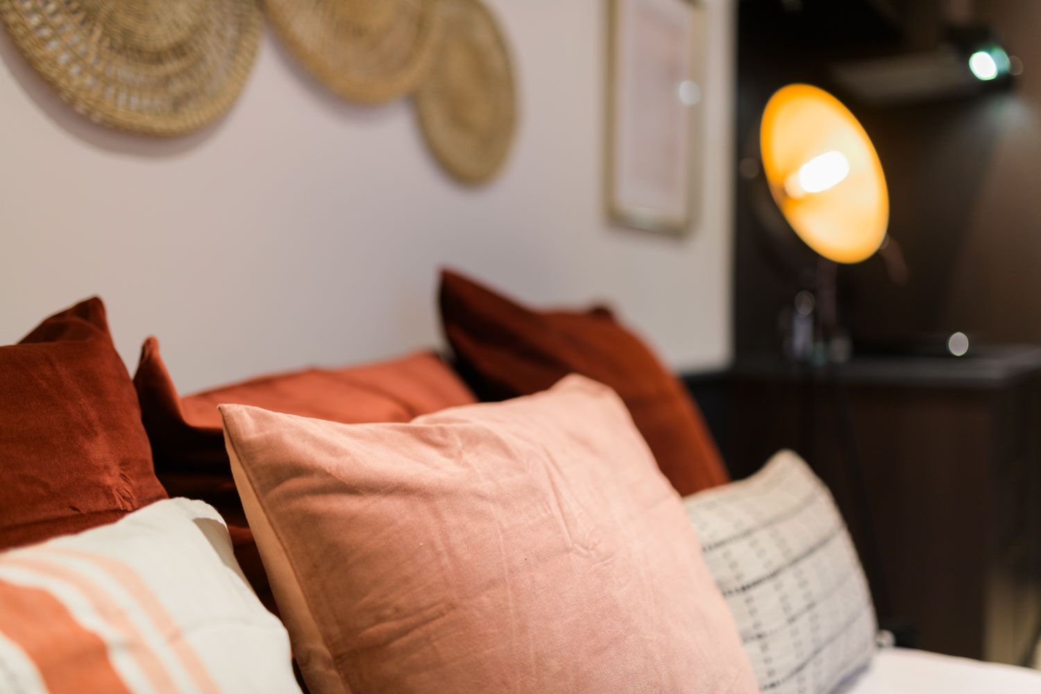 Ein Bett mit mehreren Kissen in verschiedenen Farben und einer Lampe im Hintergrund.