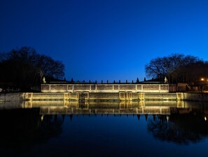 A bridge with inscriptions, surrounded by trees and a calm water body reflecting the structure. - Le Logis d'Origine. (Marly-le-Roi)