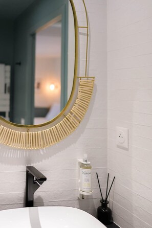 A bathroom with a white sink, a gold-framed mirror, and a bottle of soap on the wall. - Le Logis d'Origine. (Marly-le-Roi)