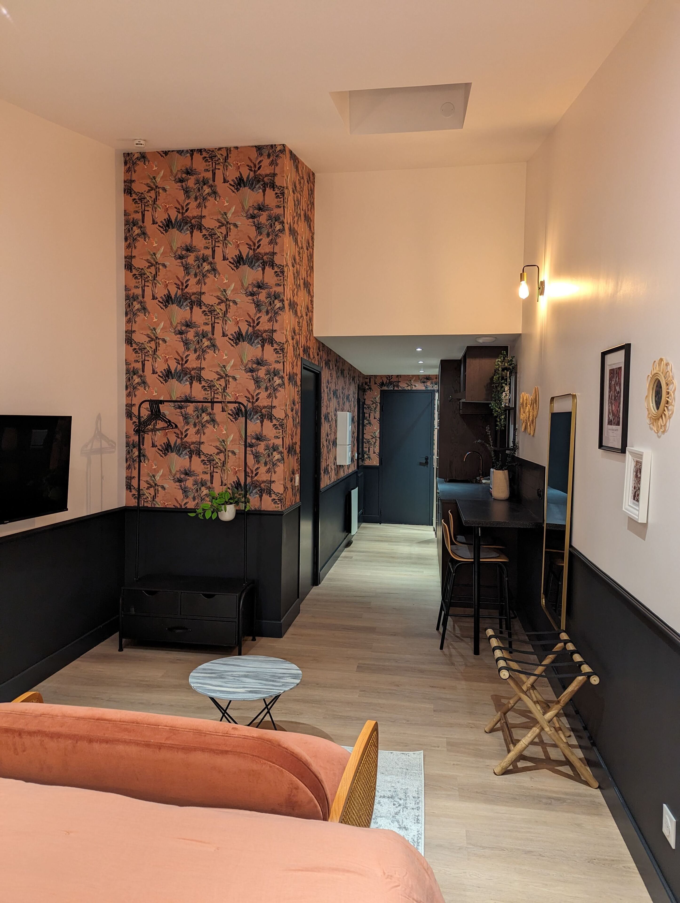 Una habitación de hotel moderna con una cama grande, un área de descanso con una mesita, un escritorio y una kitchenette al fondo.