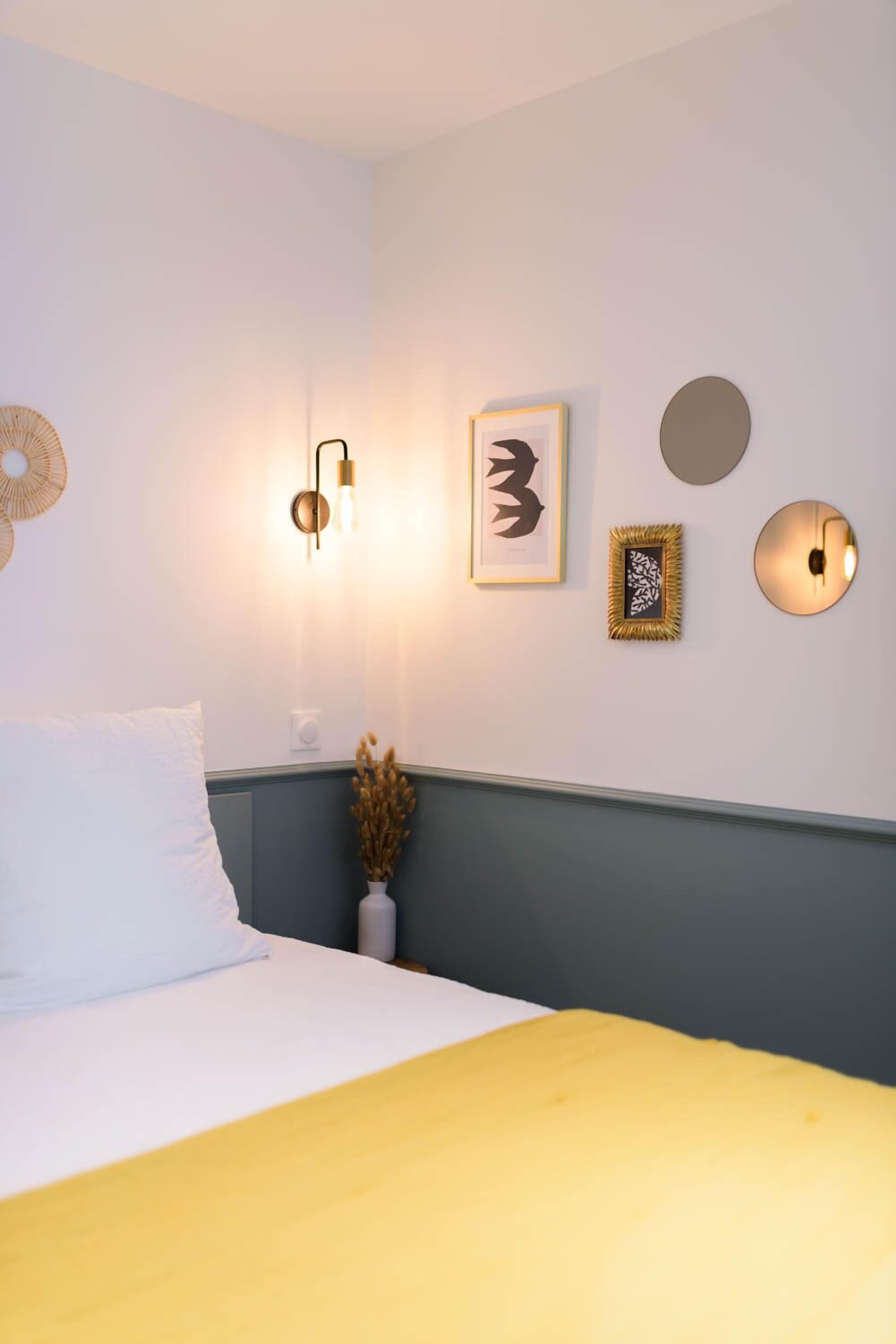 Quarto com cama, luminária fixada na parede e quadros.