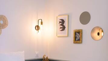 Quarto com cama, luminária fixada na parede e quadros.