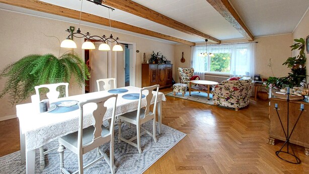 A dining area with a white table and chairs, a patterned rug, and a wooden ceiling.