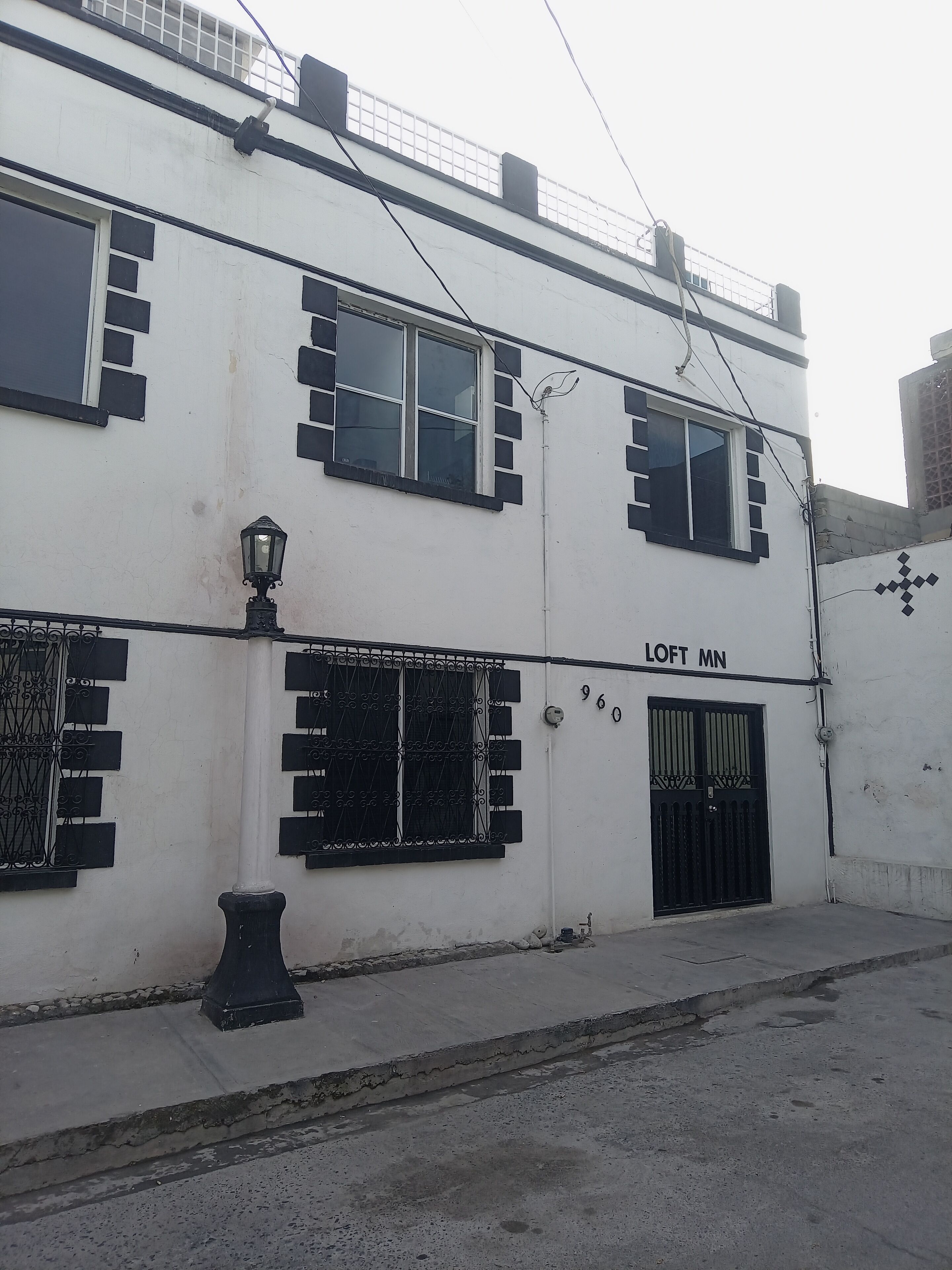 Un bâtiment blanc avec de nombreuses fenêtres, un portail noir et une enseigne indiquant « LOFT MN ».
