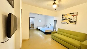 A hotel room with a green sofa, a flat-screen TV, a ceiling fan, and a painting on the wall. - DGM Lofts MTY C (Monterrey)