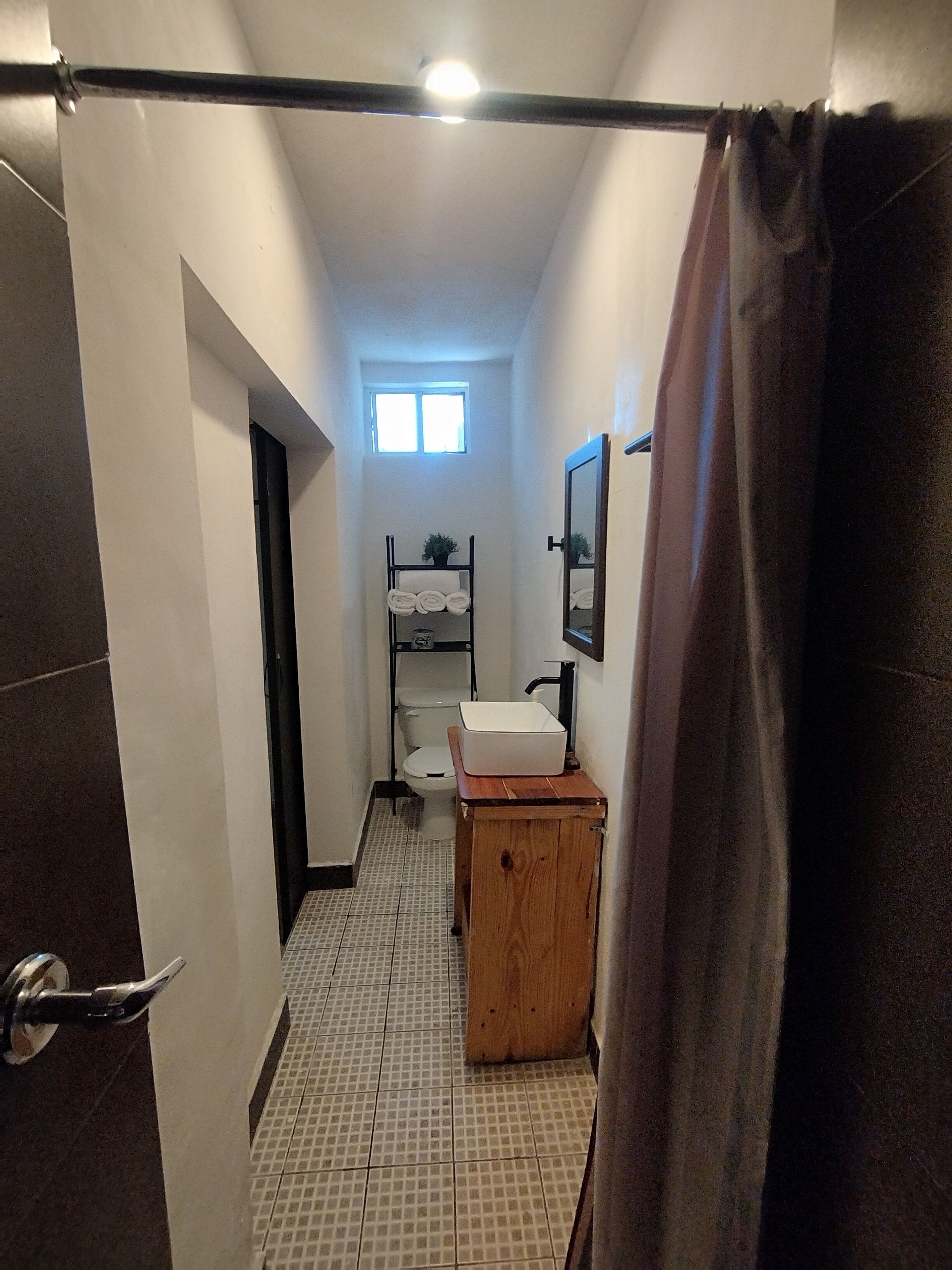 A narrow bathroom with a toilet, a sink, and a small wooden cabinet.