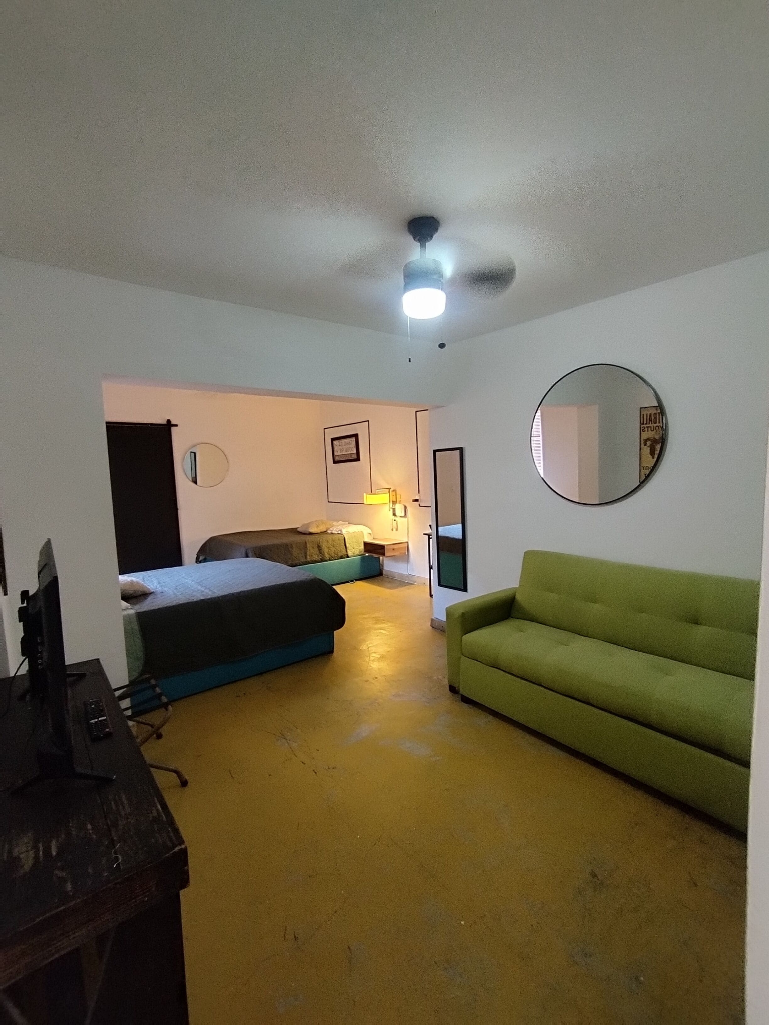 A room with a bed, a green sofa, a desk with a computer, a mirror, and a ceiling light.