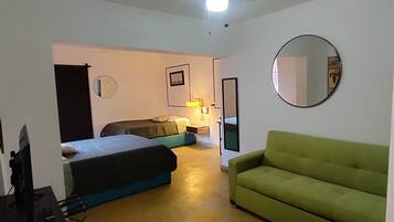 A room with a bed, a green sofa, a desk with a computer, a mirror, and a ceiling light.