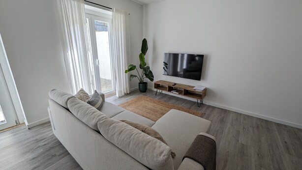 A modern living room with a large sofa, a flat-screen TV, a wooden entertainment unit, and a potted plant.