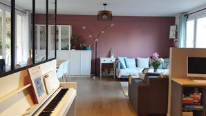 A living room with a piano, a sofa, a TV stand, and a bookshelf. - Paris, à 6mn de St Lazare, au Pied de la Gare, F3 Neuf, 7 Couchages max (Asnières sur Seine)