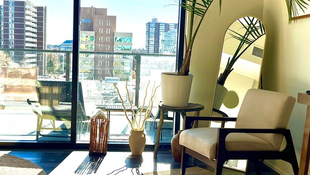 A modern living room with a large window, a chair, a small table, and a potted plant.