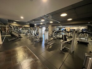 Un gimnasio con varios equipos de ejercicio, incluyendo cintas de correr y máquinas de pesas, en una distribución amplia.