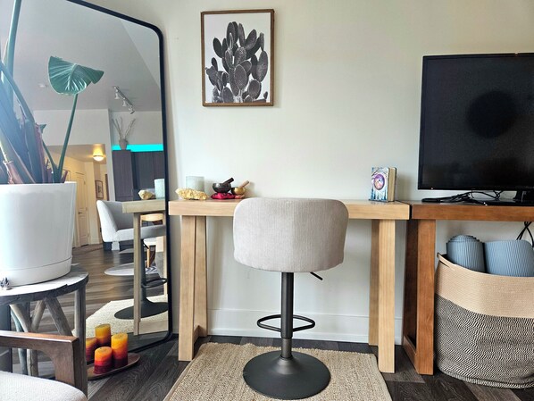 Un salon moderne avec un bureau en bois, un fauteuil de bureau noir, un téléviseur et un grand miroir.
