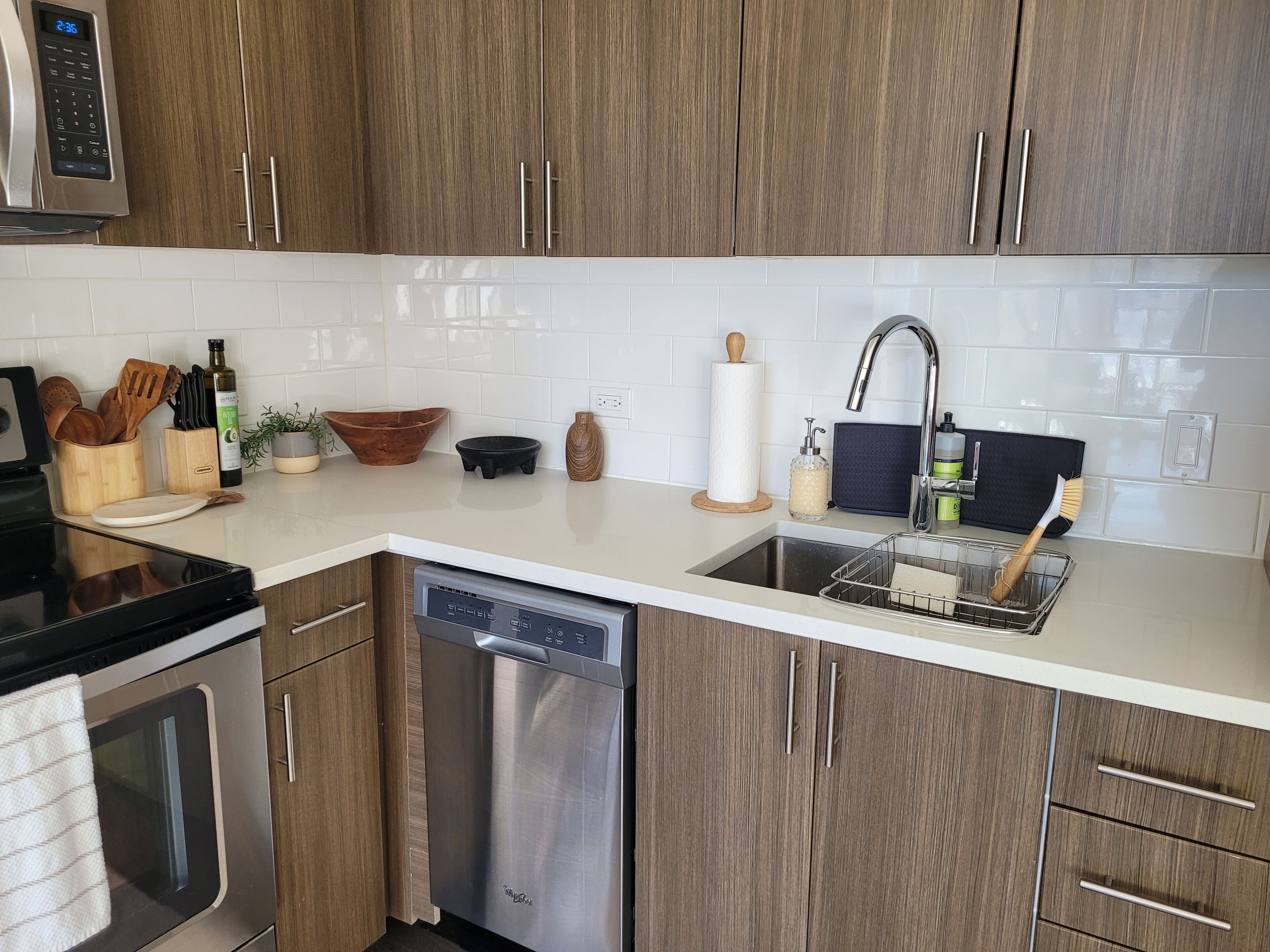 Een moderne keuken met houten kasten, een roestvrijstalen vaatwasser, een spoelbak met afwassysteem en diverse keukenbenodigdheden en apparaten.