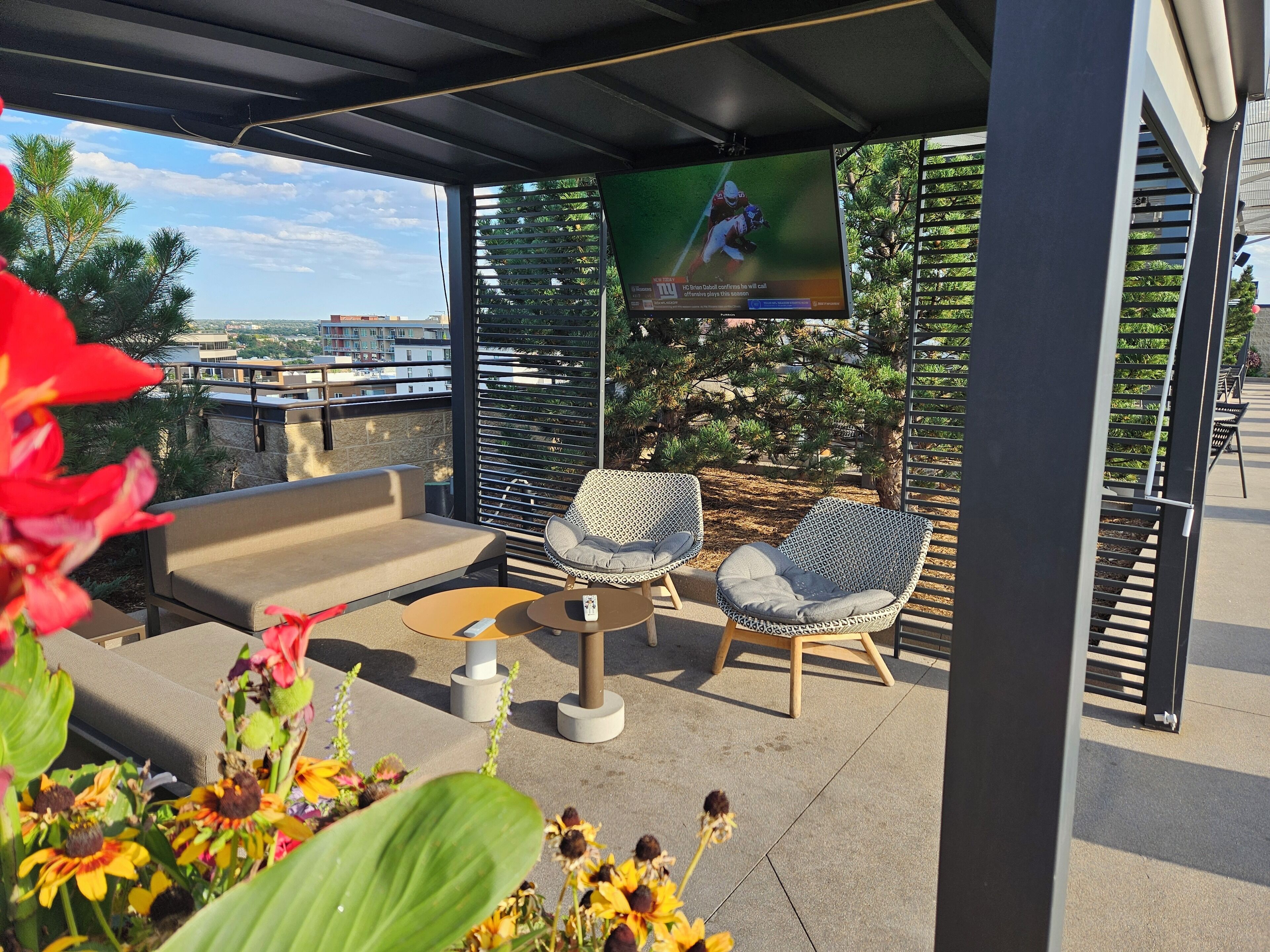 A rooftop patio with outdoor seating, a TV screen, and a view of the city.