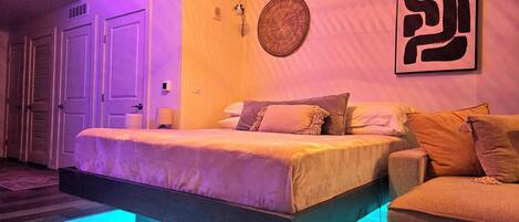 Un dormitorio con cama, una silla, una obra de arte en la pared y una puerta.