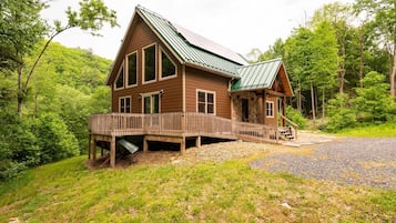 A wooden cabin with a metal roof, a deck, and a staircase leading to the entrance.