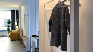 Een moderne hotelkamer met een minimalistisch design, met een houten bankje, een hangende kapstok en een klein bureau met een lamp.