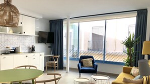 Een moderne woonkamer met een bank, een eettafel met stoelen, een aan de muur bevestigde televisie en een balkon met een hekwerk.