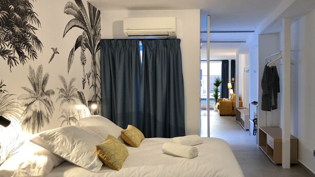 Een moderne slaapkamer met een groot bed, een wandairconditioner en uitzicht op de woonkamer.