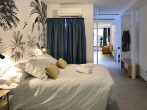 A modern bedroom with a large bed, a wall-mounted air conditioner, and a view into the living area. - ChezmoiHomes Patio De Luz 1 (Granada)