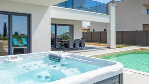 Een modern buitenzwembad met een jacuzzi, ligbedden en een eethoek.