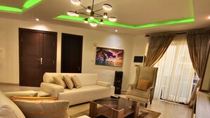 A modern living room with a sofa, coffee table, and a TV stand. There is a painting on the wall and a ceiling light fixture.